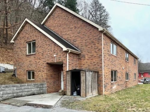 Brick two story duplex with a wooden shed and concrete driveway in a rural setting hillside behind small front entrance porch